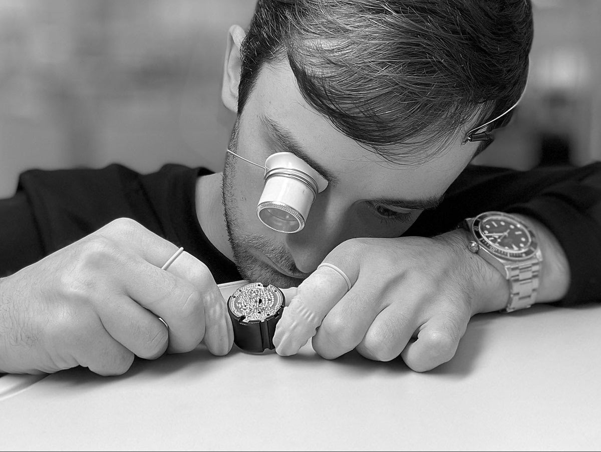 A watchmaker at the bench, working under a loupe.